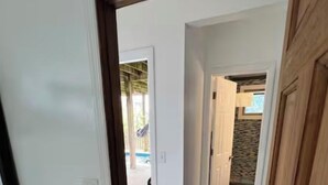A bedroom with a bed, a hallway leading to a bathroom, and a view of a pool area. - Gatsby’s Main Level. Ocean Bay Park. 
Heated Saltwater Pool + Hot Tub. Sleeps 14 (Ocean Beach)