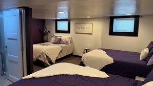 A bedroom with two beds, a small table, and a window with blinds.