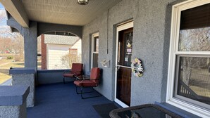 A covered porch with two red chairs, a wicker table, and a welcome sign.