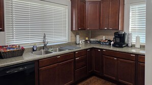 A kitchen with dark wooden cabinets, a stainless steel sink, a coffee maker, and a basket of snacks.