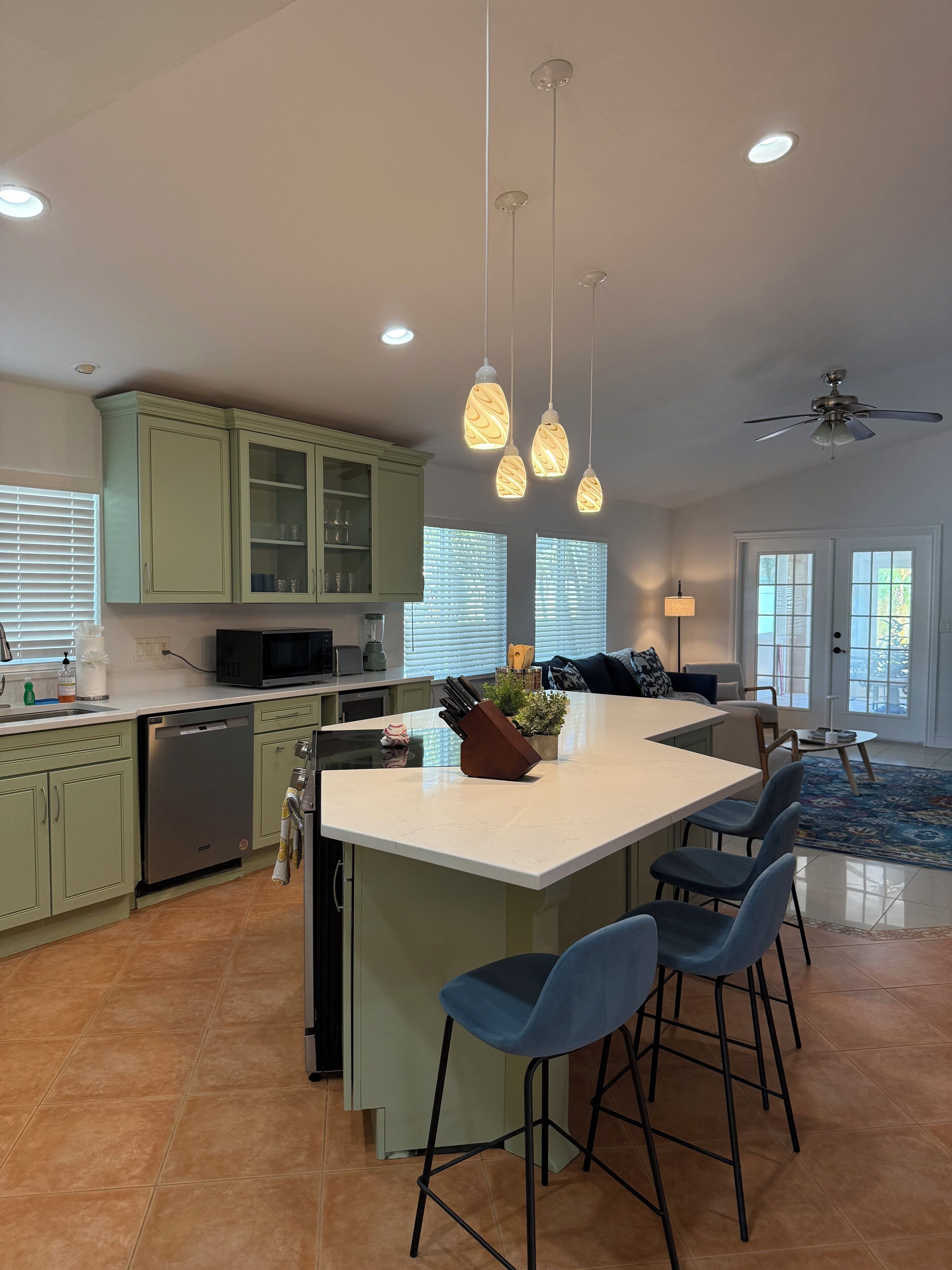 A modern kitchen with green cabinets, a central island with bar stools, pendant lighting, and a ceiling fan.