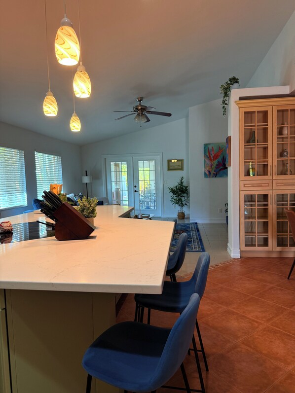 A spacious kitchen with a large island, blue chairs, pendant lights, and a ceiling fan.
