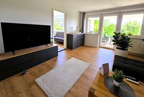 A modern living room with a flat-screen TV, a sofa, a coffee table, a rug, and a potted plant.