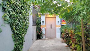 A narrow pathway leading to a door, surrounded by dense foliage and a white wall. - Umah Landuh, Spacious and comfortable private house near Ubud city (Bali)