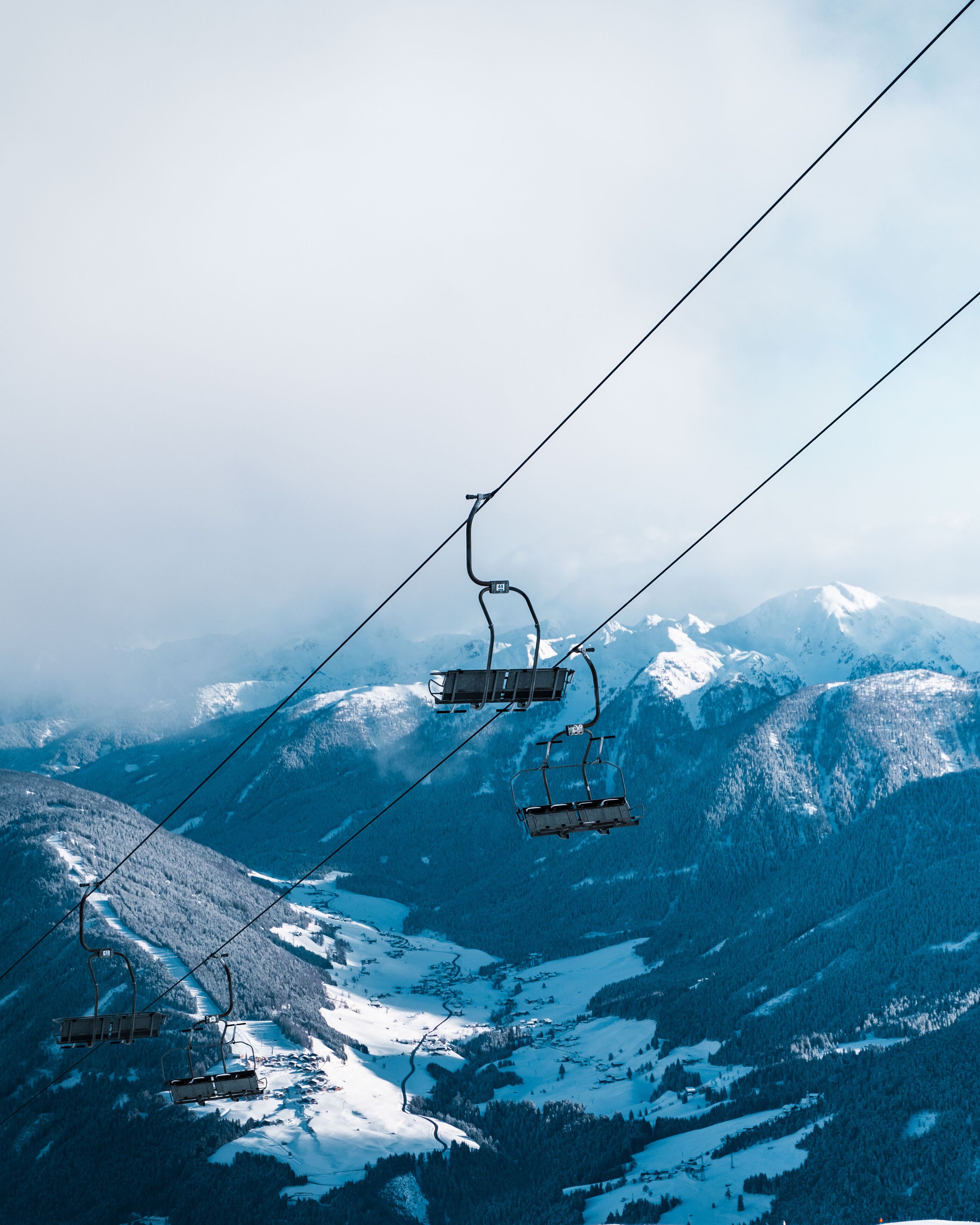 Um teleférico de esqui com cadeiras movendo-se sobre uma paisagem montanhosa coberta de neve.