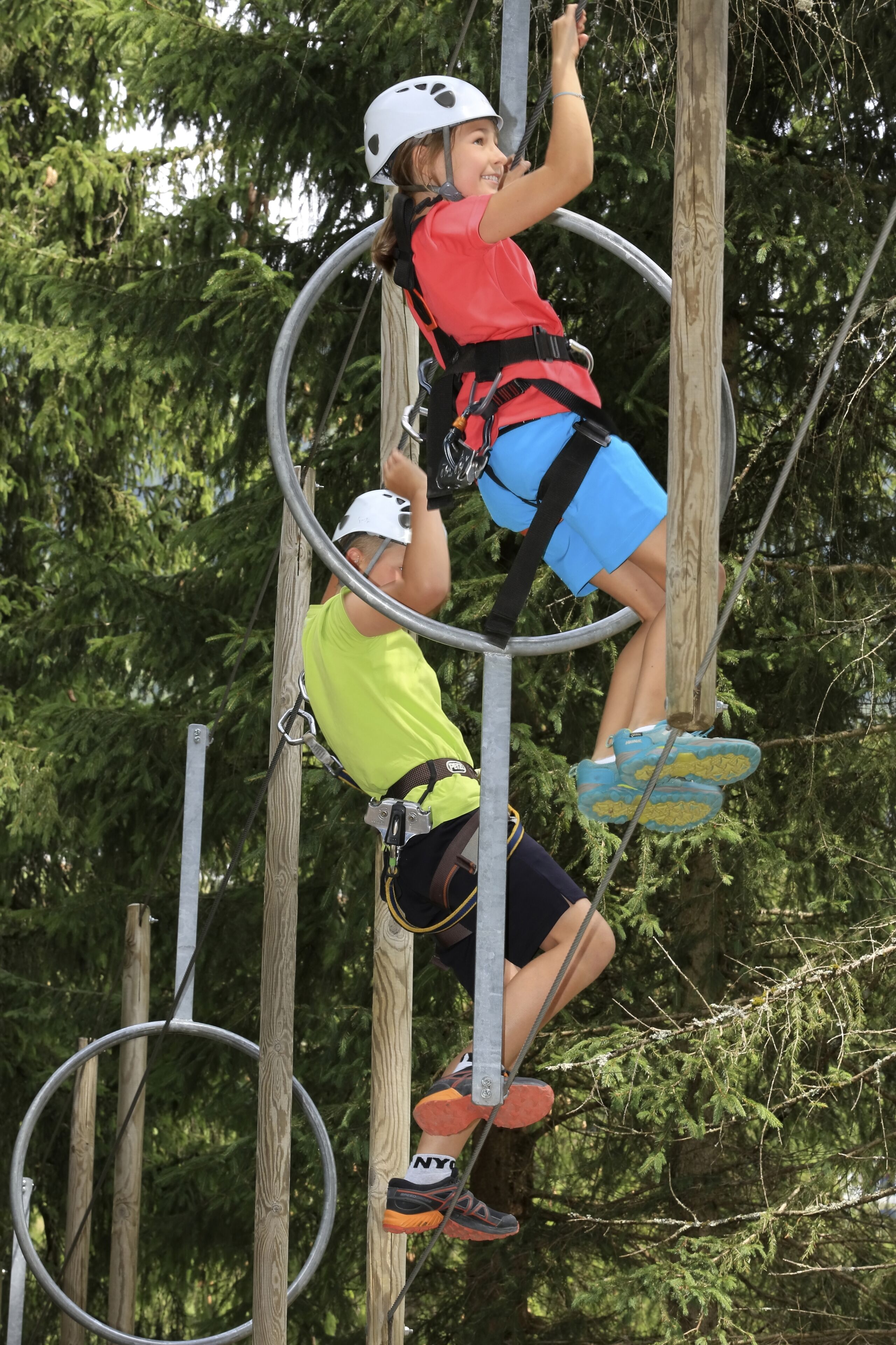 Two people engaged in an outdoor activity, climbing a wooden structure with metal rings.