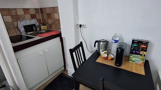 A small kitchen with a sink, stove, and cabinets. There is a dining table with chairs and a kettle on it. - Magnificent studio Montrouge (Montrouge)