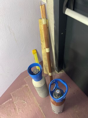 Two gas cylinders with blue caps on a surface, a wooden stick with copper wires, and a white pipe.