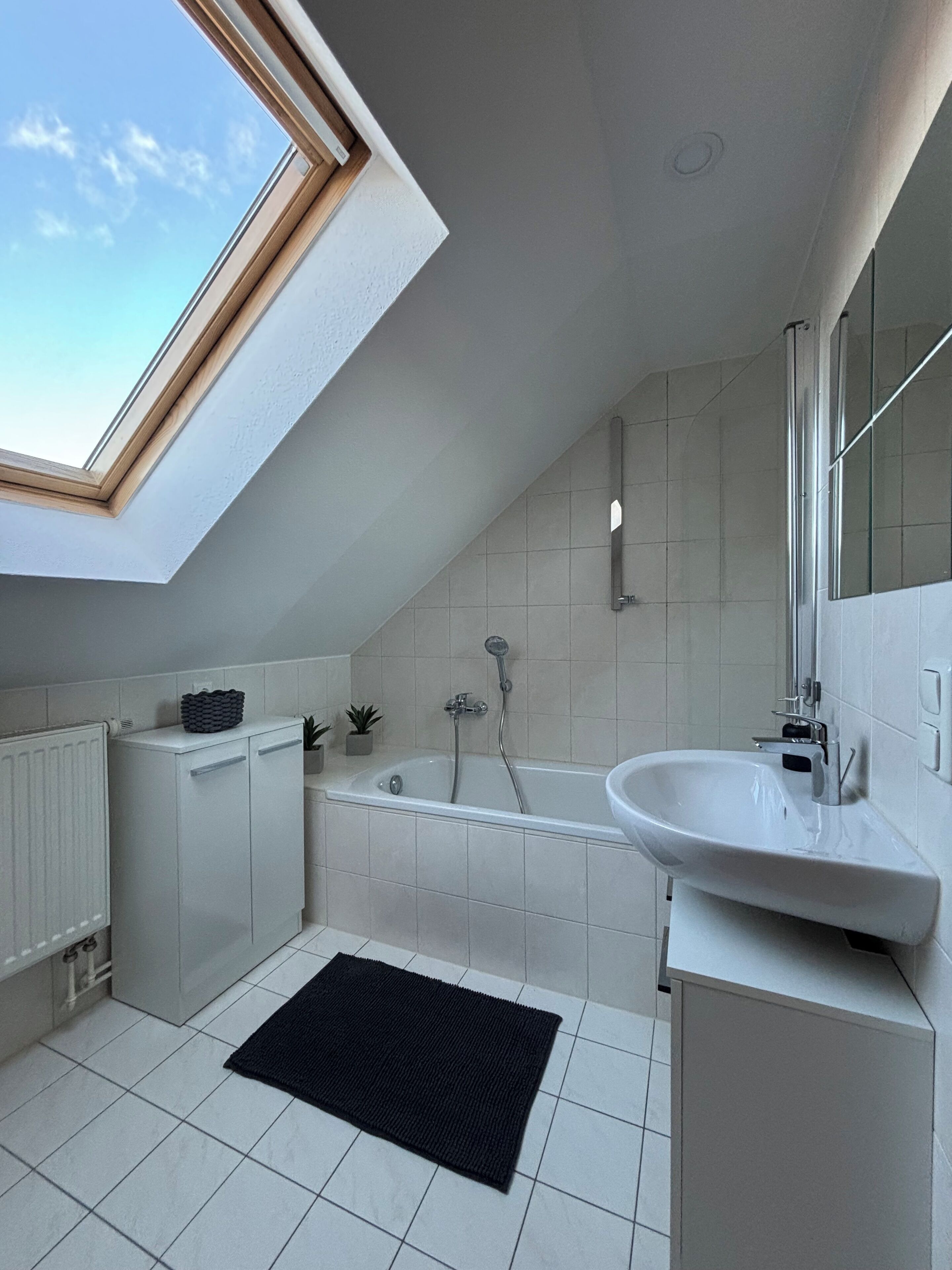 Un baño moderno con tragaluz, bañera, lavamanos y radiador.