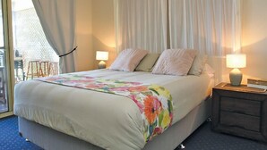 Habitación de hotel con una cama, dos lámparas de noche, una mesita y vistas al exterior.