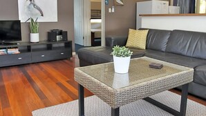 Una sala de estar moderna con un sofá, una mesa de centro de vidrio con una planta, un televisor y una estantería.