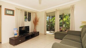 A living room with a flat-screen TV on a dark wooden TV stand, a ceiling fan, and a large window with curtains. - Relaxing waterfront property with own jetty and magnificent views (Amity Point)