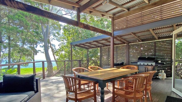 An outdoor dining area with a wooden table and chairs, a grill, and a view of the ocean. - Contemporary Beach House in waterfront location (Amity Point)