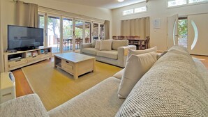A spacious living room with a flat-screen TV, a sofa, a coffee table, and a dining area with chairs and a table. - Contemporary Beach House in waterfront location (Amity Point)
