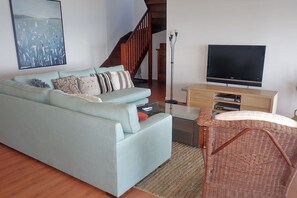 Una sala de estar con un sofá azul claro, un sillón de mimbre, un televisor de pantalla plana y una escalera de madera.