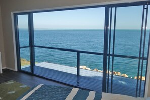 Une pièce dotée d’une grande porte-fenêtre coulissante donnant sur un balcon avec vue sur une étendue d’eau.