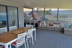 Une terrasse extérieure avec une table et des chaises en bois, un barbecue intégré et un coin salon confortable agrémenté de coussins.