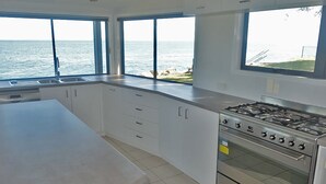 A modern kitchen with large windows, a gas stove, and white cabinetry. - Large waterfront home with bay views to Moreton Island (Amity Point)