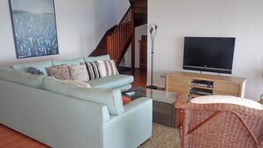 A living room with a light blue sofa, a wicker chair, a flat-screen TV, and a wooden staircase. - Large waterfront home with bay views to Moreton Island (Amity Point)