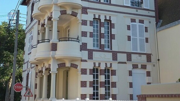 A multi-story building with a white facade and red brick accents, featuring balconies and a chimney. - Ground floor apartment in old villa 60 m from the beach (Cabourg)