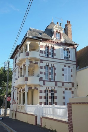Un immeuble à plusieurs étages, doté d’une façade blanche et de détails en briques rouges, avec des balcons et une cheminée.