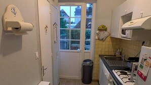 A narrow kitchen with a window, a microwave, a sink, and a trash bin. - Ground floor apartment in old villa 60 m from the beach (Cabourg)