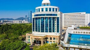 A modern building with a dome and glass facade, surrounded by greenery and other buildings. - Shanghai Hotel (Shenzhen)
