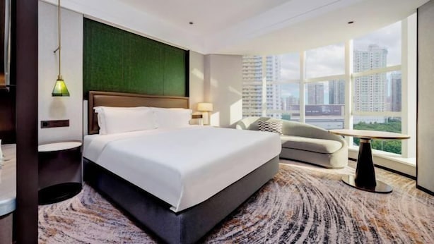 A hotel room with a large bed, a sofa, a small table, and a view of the cityscape. - Shanghai Hotel (Shenzhen)