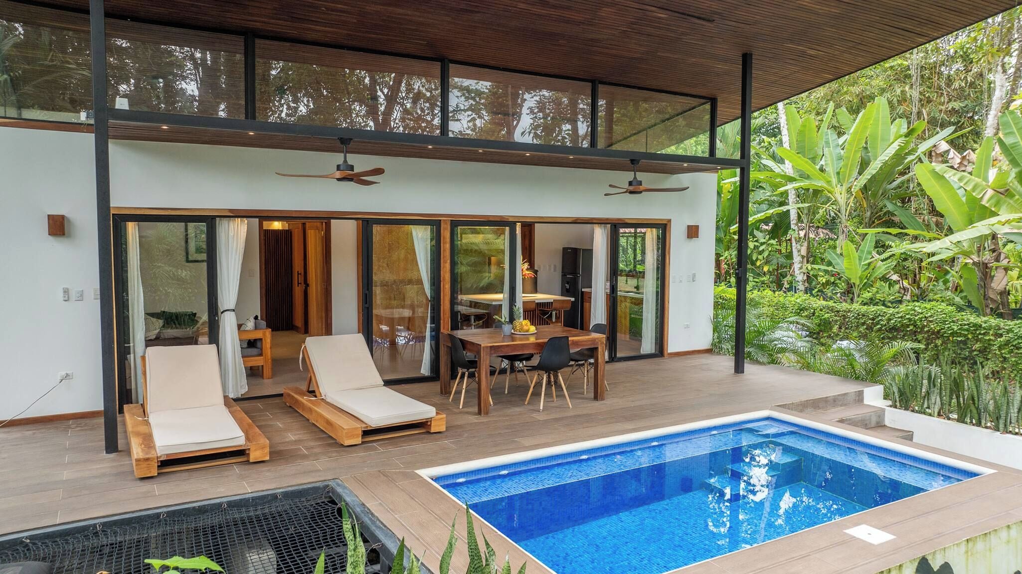 A modern outdoor pool area with a dining table and lounge chairs.