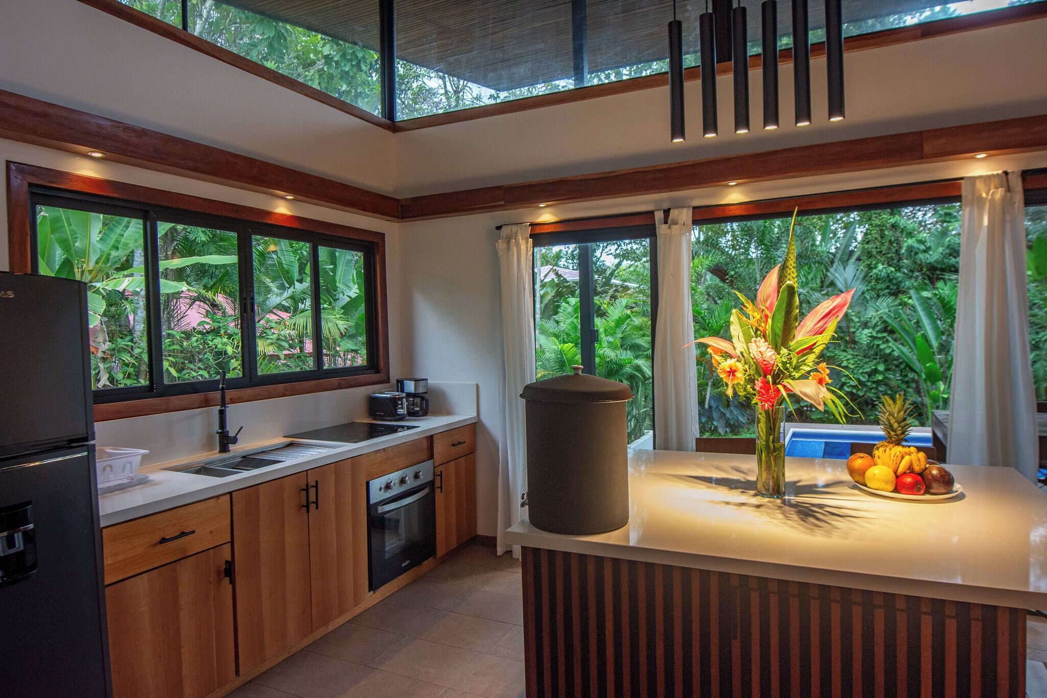 A modern kitchen with a large window, a built-in oven, and a countertop with a fruit bowl.