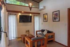 A room with a wooden sofa, a small table, a TV, and two framed pictures on the wall.
