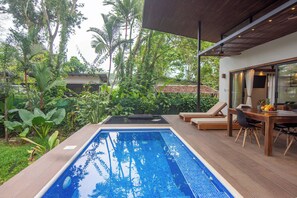 A swimming pool with lounge chairs and a dining area, surrounded by lush greenery.