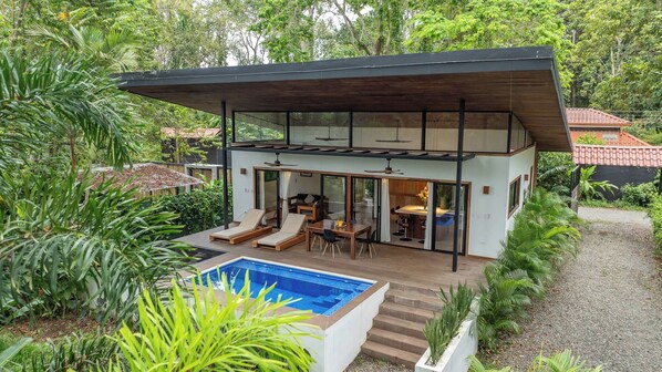 A modern two-story house with a pool, outdoor seating, and lush greenery.