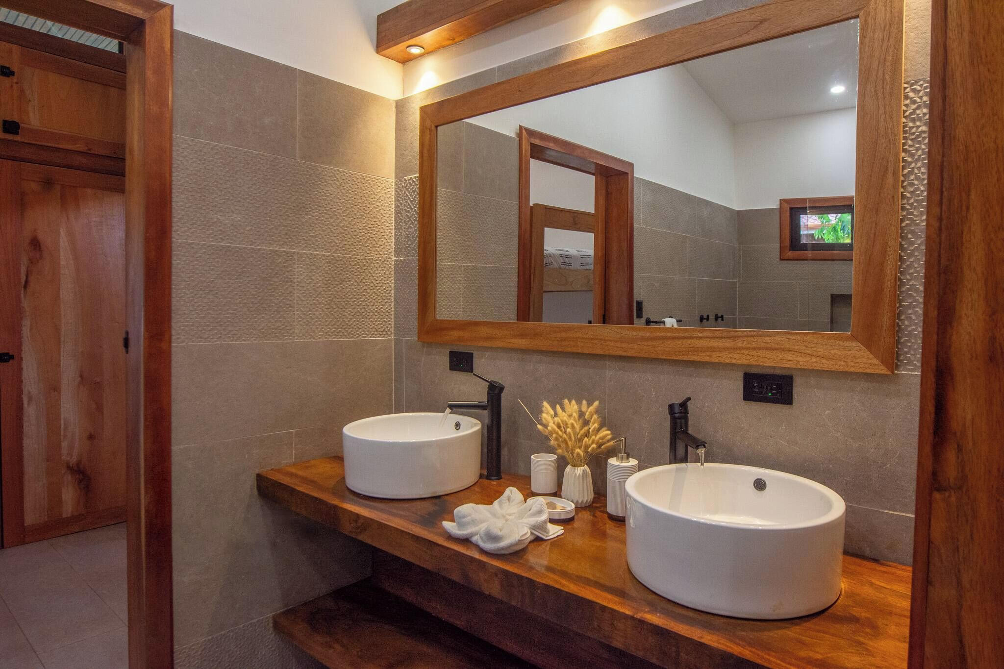 A bathroom with two round sinks, a wooden vanity, a large mirror, and a towel on the counter.