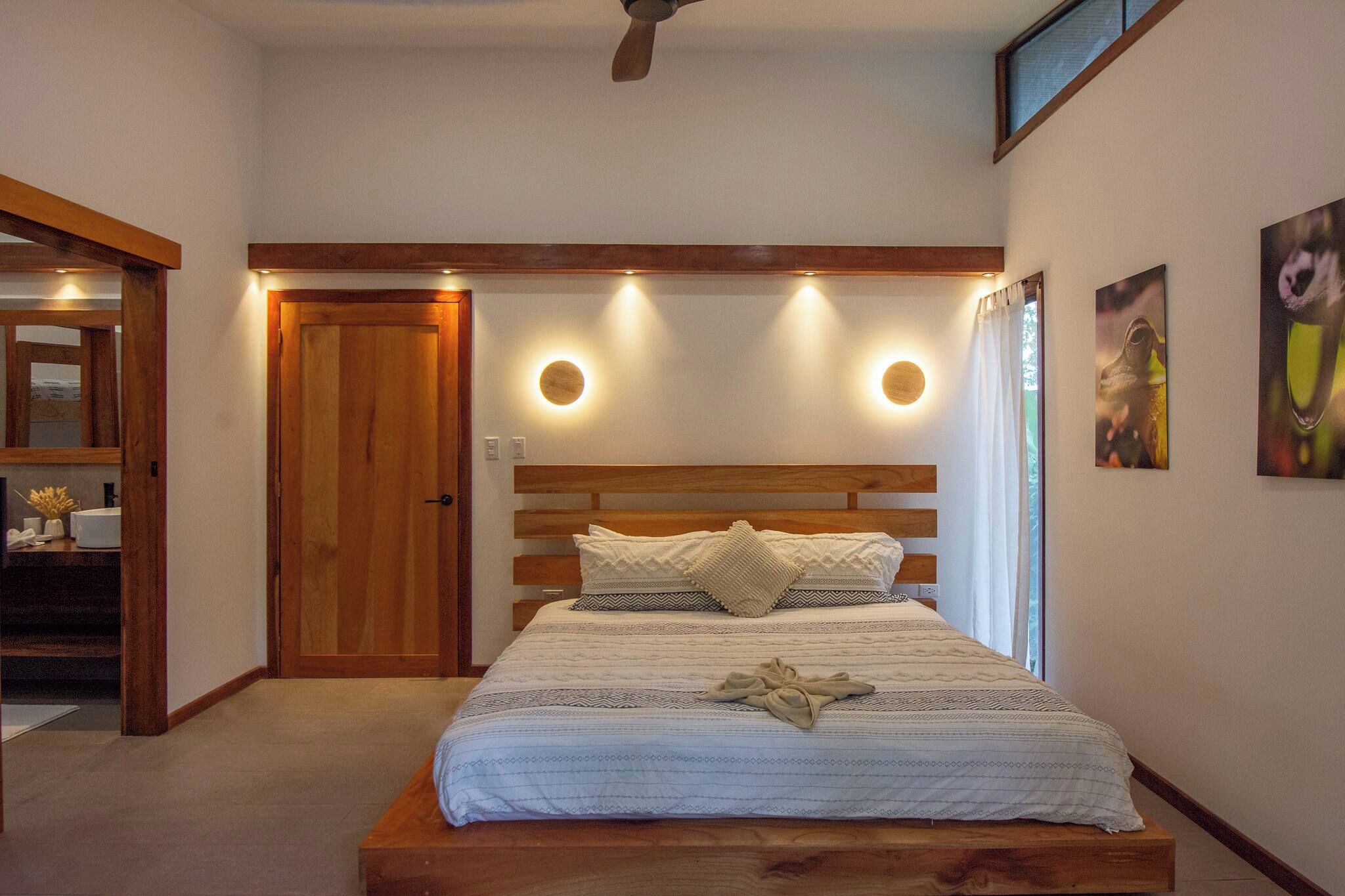 A bedroom with a wooden headboard, a bed with patterned bedding, a bedside table, and a ceiling fan.