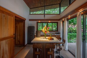 A modern kitchen with a central island, wooden cabinetry, and a large window offering a view of greenery.