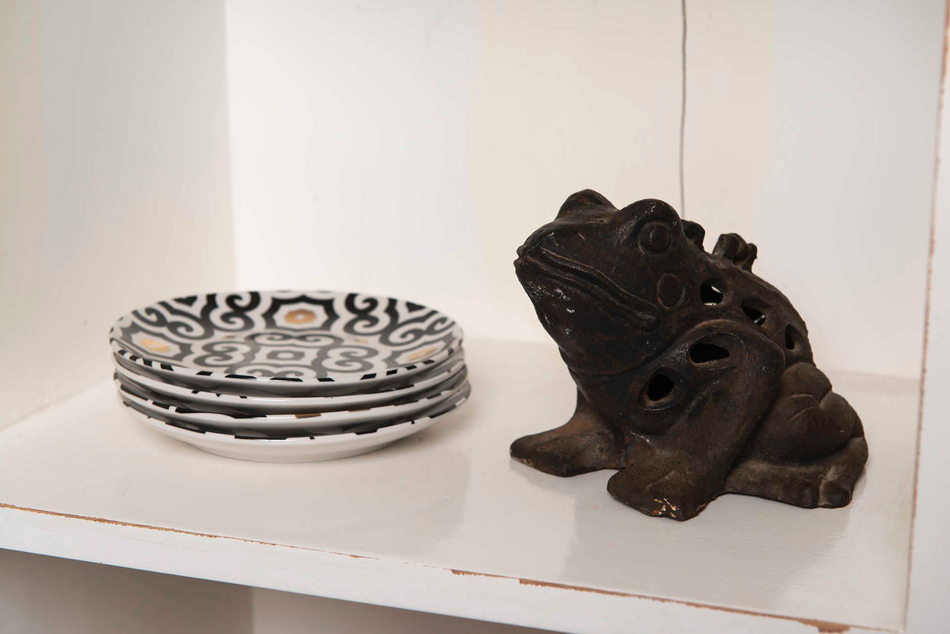 A stack of patterned plates and a ceramic frog figurine on a white shelf.