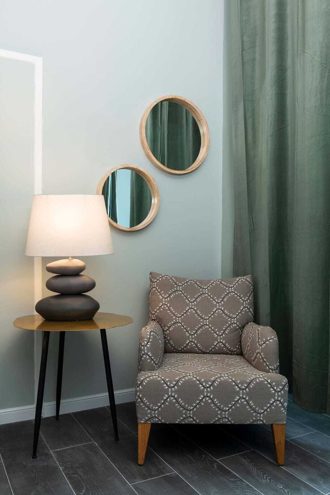 Une chaise recouverte d’un tissu à motifs, une table ronde avec une lampe et deux miroirs fixés au mur.