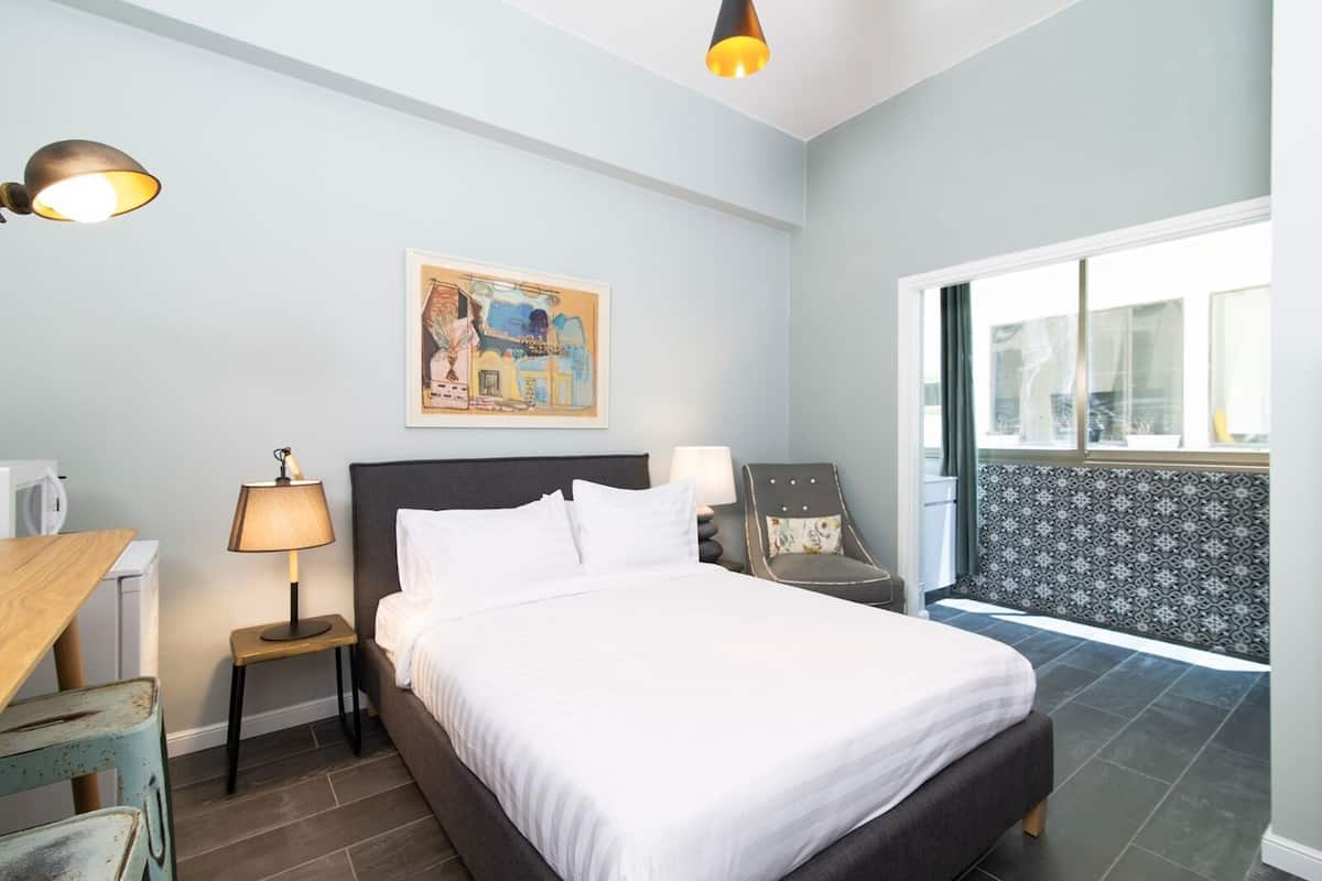 A hotel room with a bed, bedside lamps, a chair, a painting, and a view of the outside.