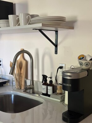 Une cuisine équipée d’un évier, d’une machine à café et d’une étagère où sont rangées des tasses et des assiettes.