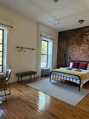 Une chambre à coucher avec un lit, un banc, une chaise, un radiateur et un mur en briques.