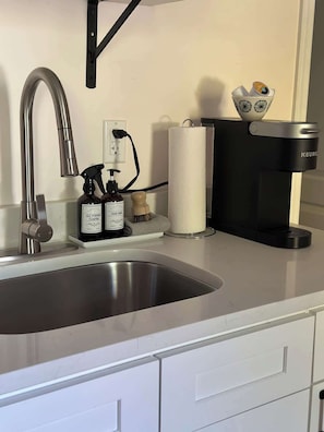 Ett kök med en diskho i rostfritt stål, en kaffebryggare och en hållare för hushållspapper.