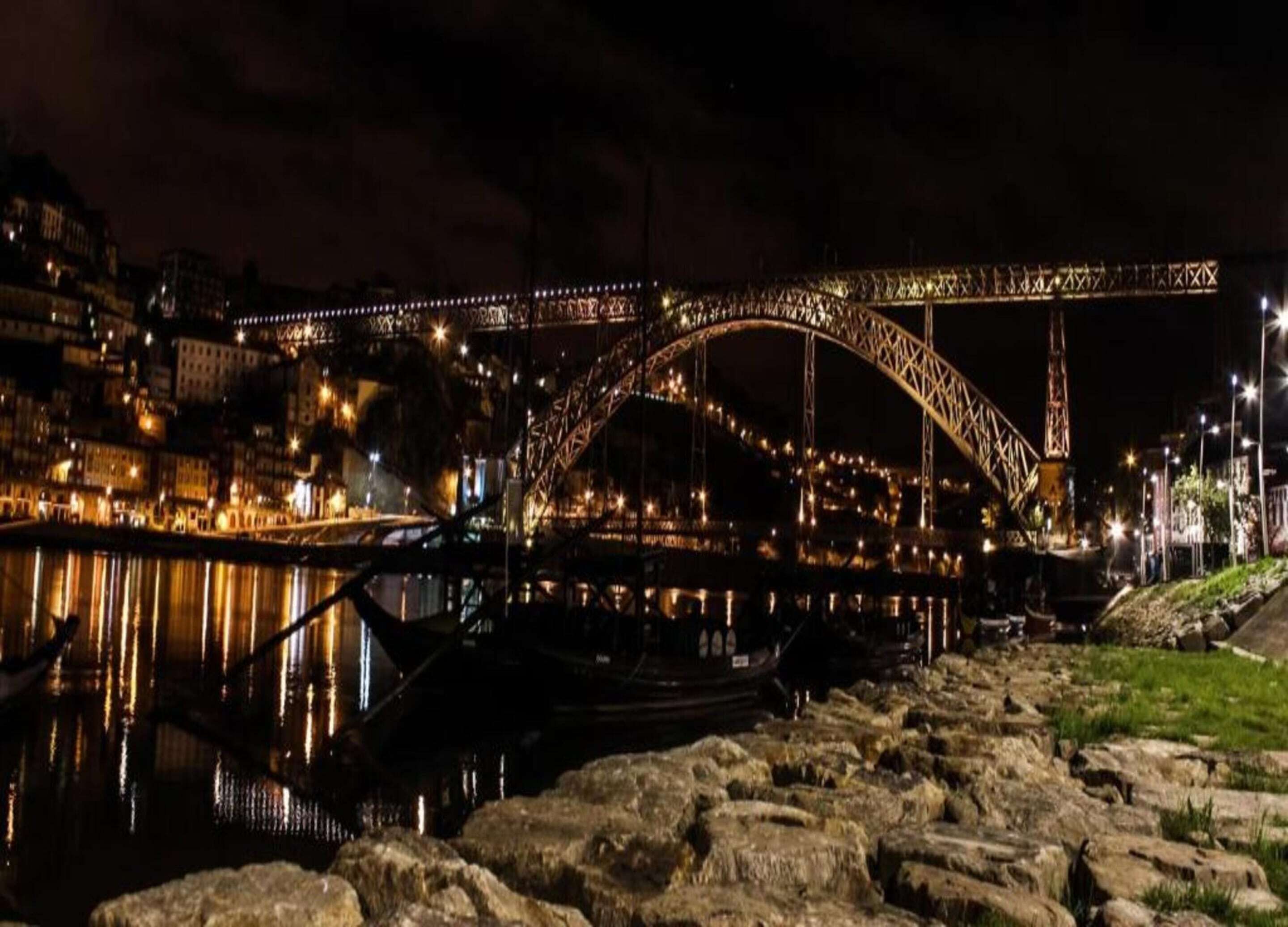 Una vista nocturna de un puente iluminado, un río y barcos.