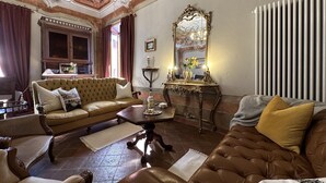 A spacious living room with a large sofa, a smaller sofa, and a brown leather couch. There is a wooden coffee table, a floor lamp, and a decorative mirror on a console table.