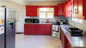 Une cuisine moderne avec des meubles rouges, des appareils en acier inoxydable et une fenêtre qui laisse entrer la lumière naturelle.