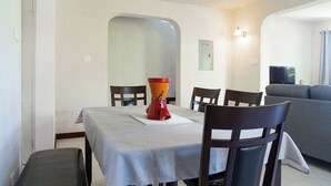 Un coin repas avec une table dressée pour deux personnes, un vase rouge et un canapé gris en arrière-plan.