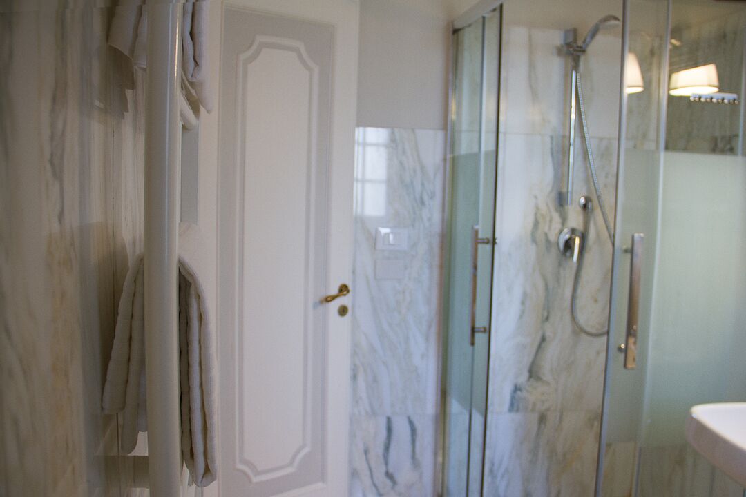 Un bagno con cabina doccia in vetro, parete in marmo e porta bianca.