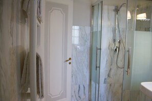 A bathroom with a glass-enclosed shower, a marble wall, and a white door. - Le Duchesse Rooms and Events (Trani)