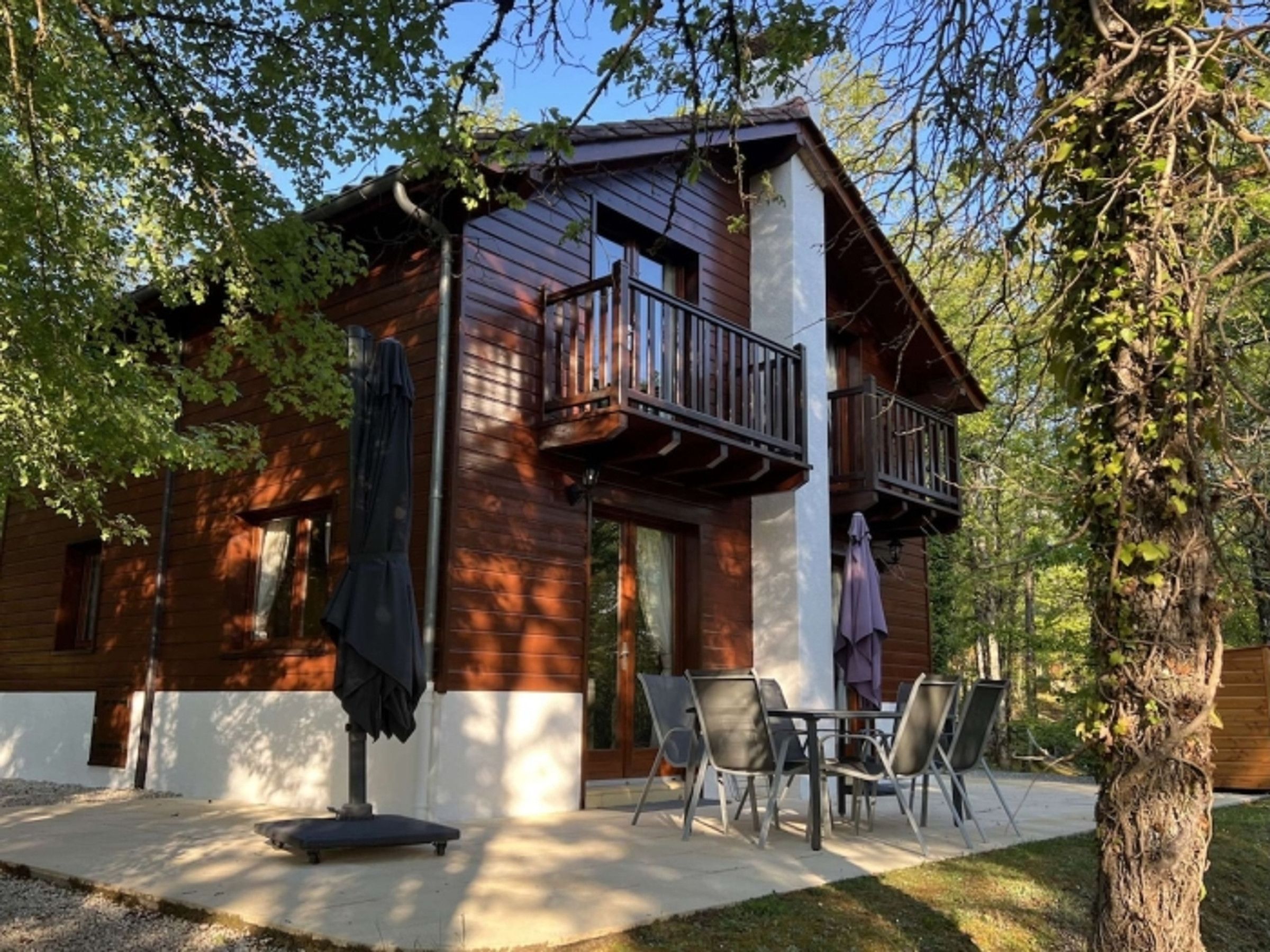 Une cabane en bois dotée d’un balcon, d’un espace salon extérieur et d’un arbre au premier plan.