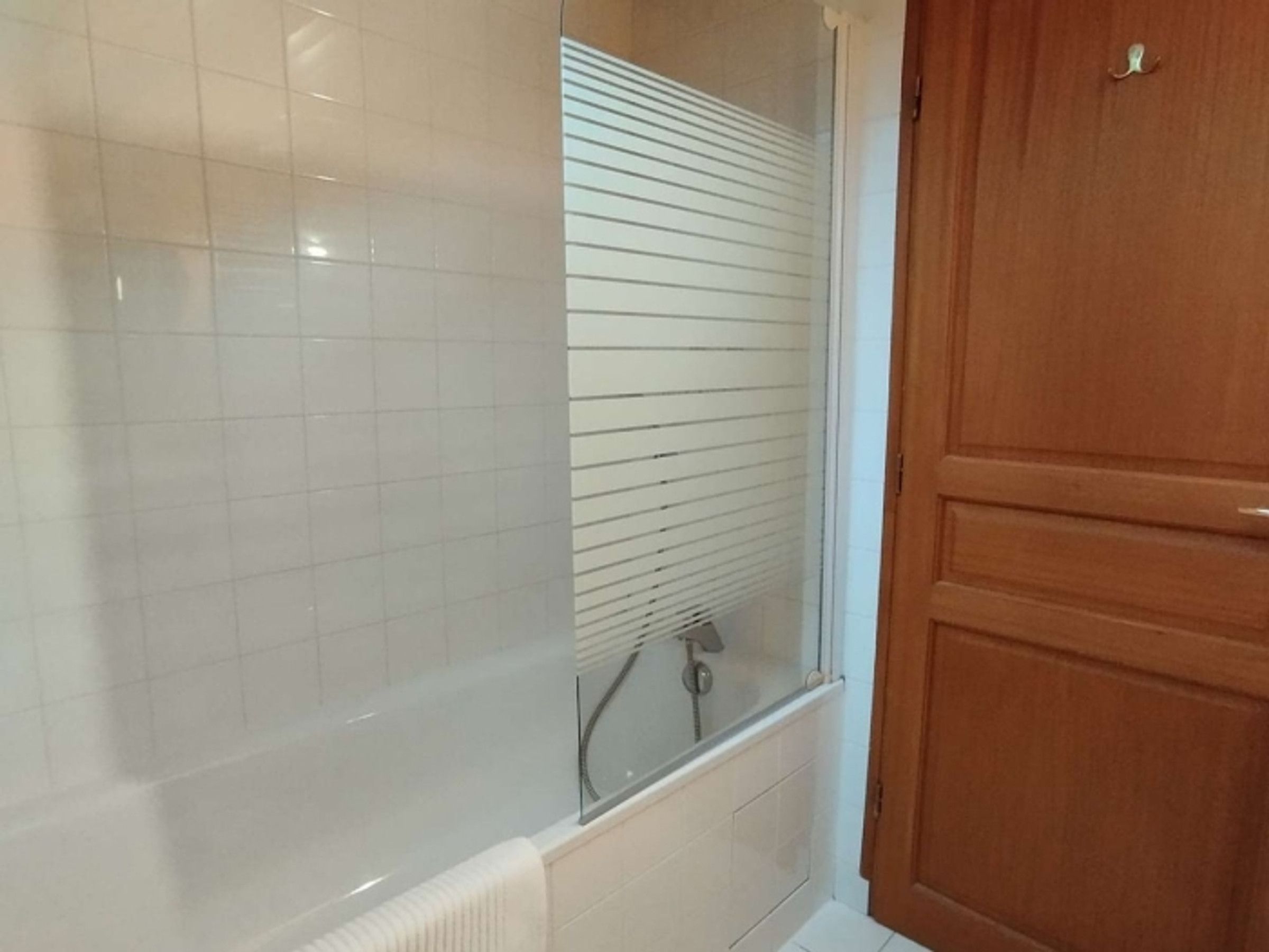 Een badkamer met een douchecabine, een houten deur en betegelde wanden.